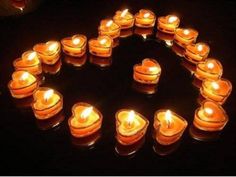 many lit candles arranged in the shape of a heart on a black surface with words written below