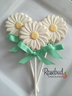 three white flowers with green ribbons on top of each other in the shape of a heart