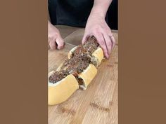 a person cutting up a long hot dog on a wooden board with a knife in it