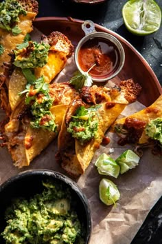 some tacos and guacamole are on a plate with dipping sauces