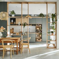 an open kitchen and dining room area with wooden table, chairs and shelves filled with potted plants