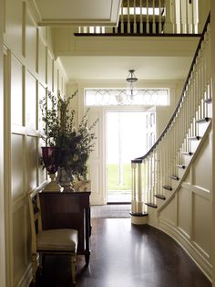 an entry way with stairs and a plant on the table in front of the door