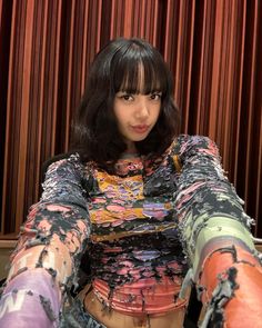 a woman with black hair and colorful clothes posing for the camera in front of a red curtain