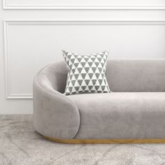 a grey couch with a pillow on it in front of a white wall and floor