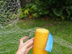 a person holding a yellow object in their hand near a netted area with grass and bushes