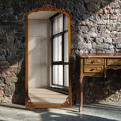 a mirror sitting on top of a wooden table next to a brick wall with a window