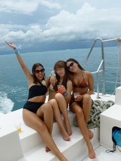 three women in bathing suits sitting on the back of a boat with their arms up