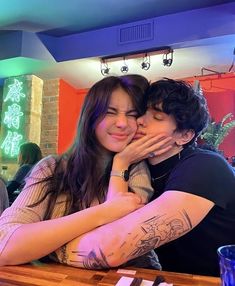 a man and woman hugging each other while sitting at a table in front of a bar