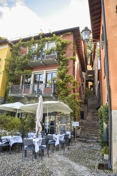 an outdoor dining area with tables and umbrellas on cobblestone pavement in front of multi - story building