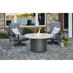 a fire pit sitting on top of a patio next to two chairs and a potted plant