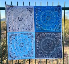 three blue and white quilts hanging on a fence