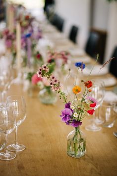 a long table is set with wine glasses and vases filled with colorful wildflowers