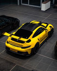 two yellow sports cars parked next to each other on a tile floor in front of a building