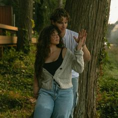 two people standing next to each other in front of a tree and one person holding his hand up