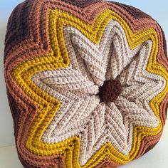 a crocheted cushion with an orange and yellow flower on the front, sitting on a white surface