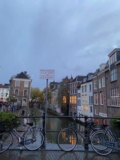 three bicycles parked next to each other on the side of a river in front of buildings