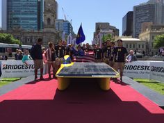 a group of people standing on top of a red carpet next to a solar panel