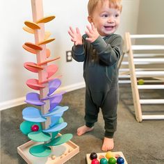 a little boy standing next to a toy tree with colorful balls on the ground in front of it