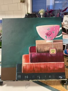 a painting of a pink cup on top of books