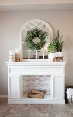 a fireplace with a wreath on top of it next to potted plants and candles