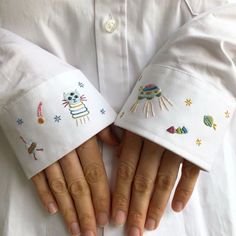 two hands wearing white embroidered hats with animals and stars on them, both holding each other