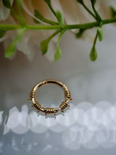 a gold ring sitting on top of a table next to a flower vase with white flowers in the background