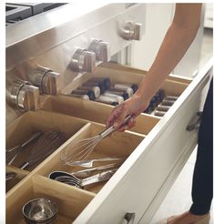 a woman is standing in front of an open drawer with utensils and pans