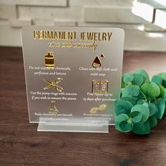 there is a sign that says permanent jewelry on the table next to some green leaves