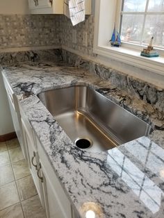 a kitchen with marble counter tops and stainless steel sink under a window in the corner