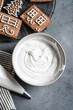 cookies decorated with icing are on a plate next to a bowl of whipped cream