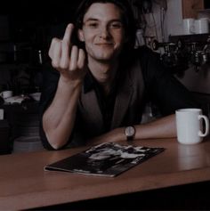 a man sitting at a table with his hand up in front of him and a coffee mug