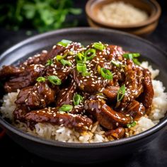 a black bowl filled with rice and meat covered in sesame seeds, garnished with green onions