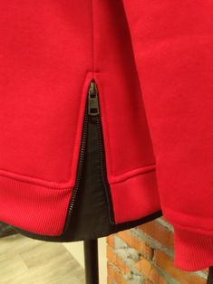 a red jacket with black zippers on the front and back, hanging up against a brick wall