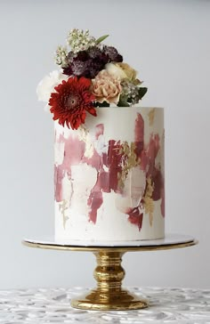 a white cake with red and pink flowers on top is sitting on a gold plate