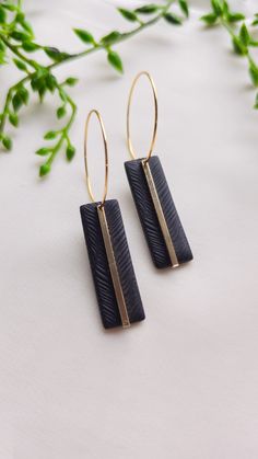 two black and gold earrings sitting on top of a white table next to green leaves