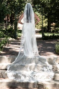 the back of a bride's dress as she stands on steps in front of trees