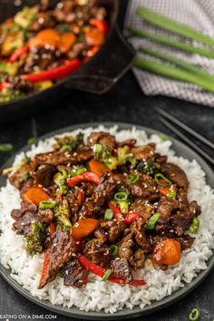 beef and vegetable stir fry served over rice on a black plate with chopsticks