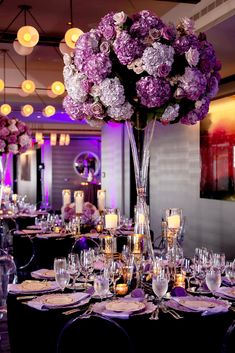 a tall vase filled with lots of purple flowers sitting on top of a dining room table