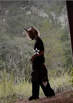 a person with a cat mask on walking in the dirt near some wires and trees