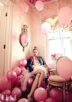 a woman sitting on a chair surrounded by balloons and streamers in a pink room