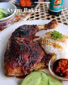 a plate with meat, rice and cucumber on it next to some sauce