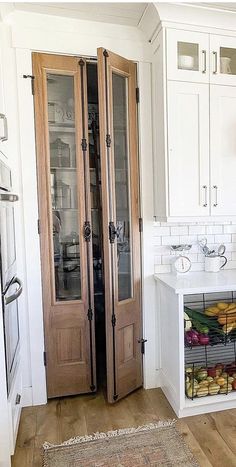 a kitchen with white walls and wooden floors has glass doors that lead into the pantry