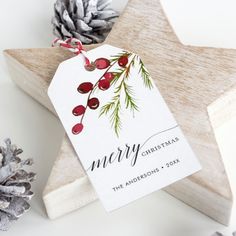 a wooden star ornament with a christmas tag on it next to pine cones