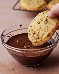 a person dipping chocolate into a cookie in a glass bowl