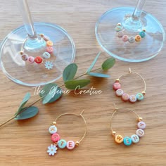 three wine glasses filled with different types of bead jewelry on top of a wooden table