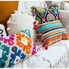 colorful pillows on a white bed with pom poms around the edges and tassels