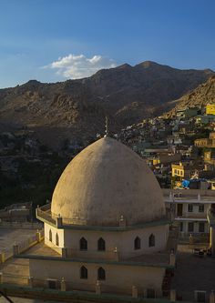 an old building in the middle of a city with mountains in the background and blue sky