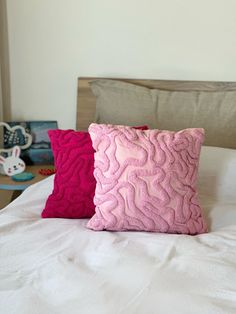 two pink pillows sitting on top of a white bed