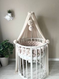 a white crib with a canopy and pillows on it next to a potted plant