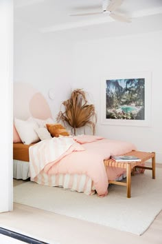 a bed with pink sheets and pillows in a white room next to a painting on the wall